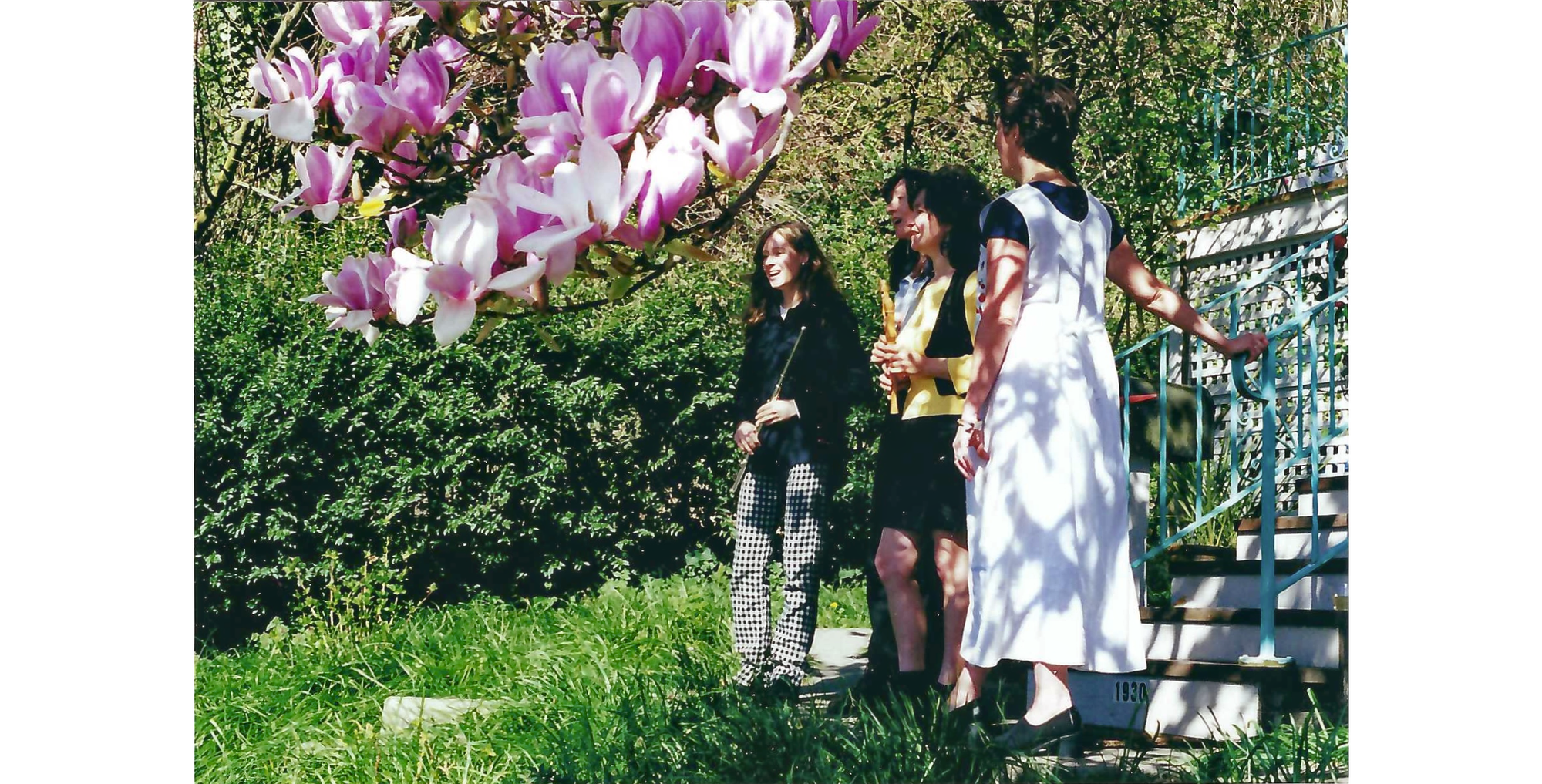 Photo of four women with instruments, singing, in front of steps with magnolia branch in foreground