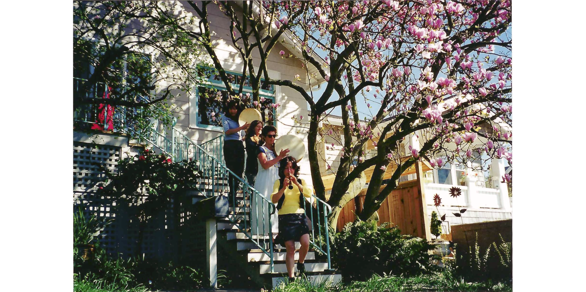 Photo of 4 women playing instruments walking down stairs with magnolia and house in background