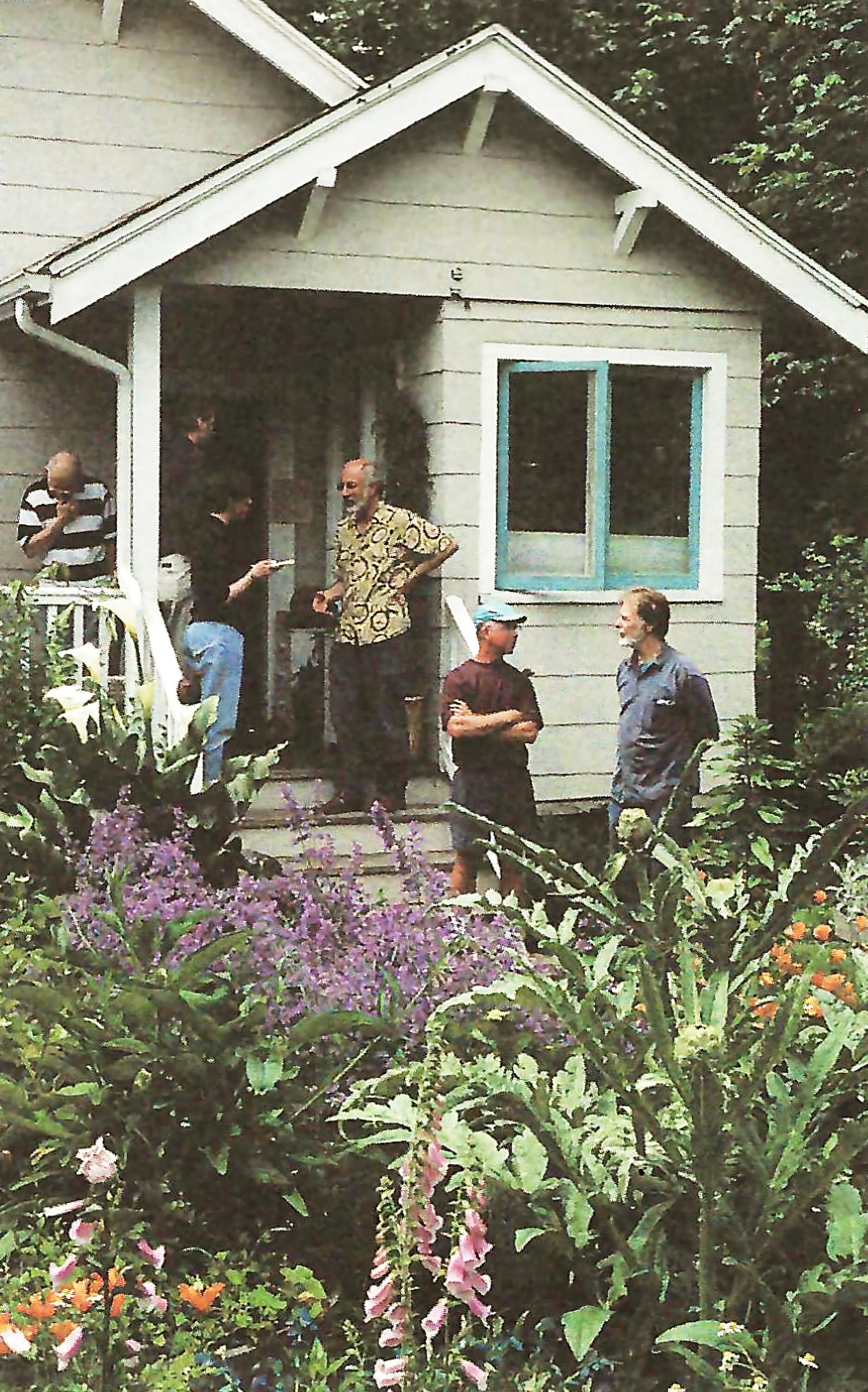 Photo of the back porch of a house facing a garden, with people standing in both places conversing.