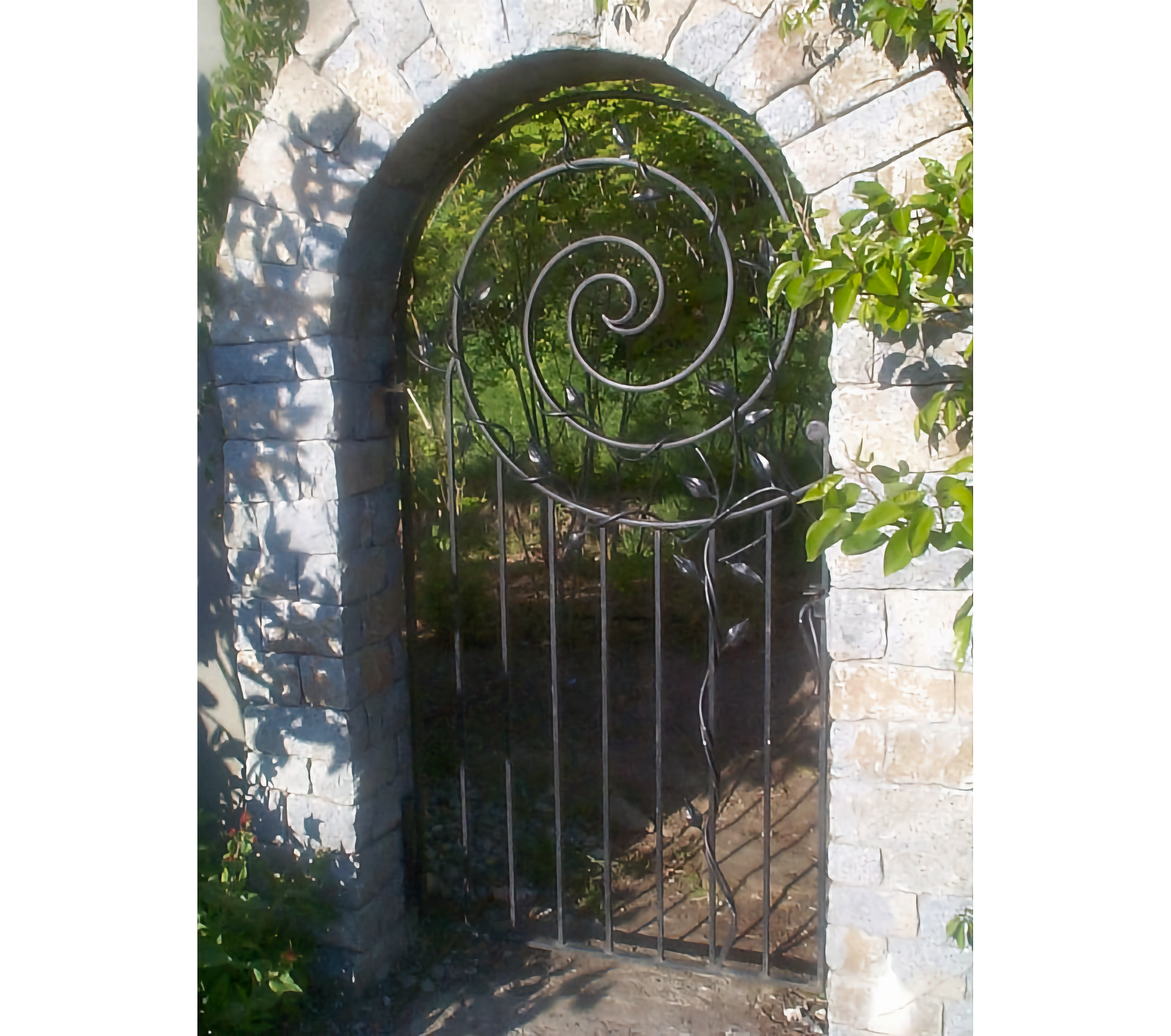 Photo of stone arch with spiral-topped iron gate leading to a garden