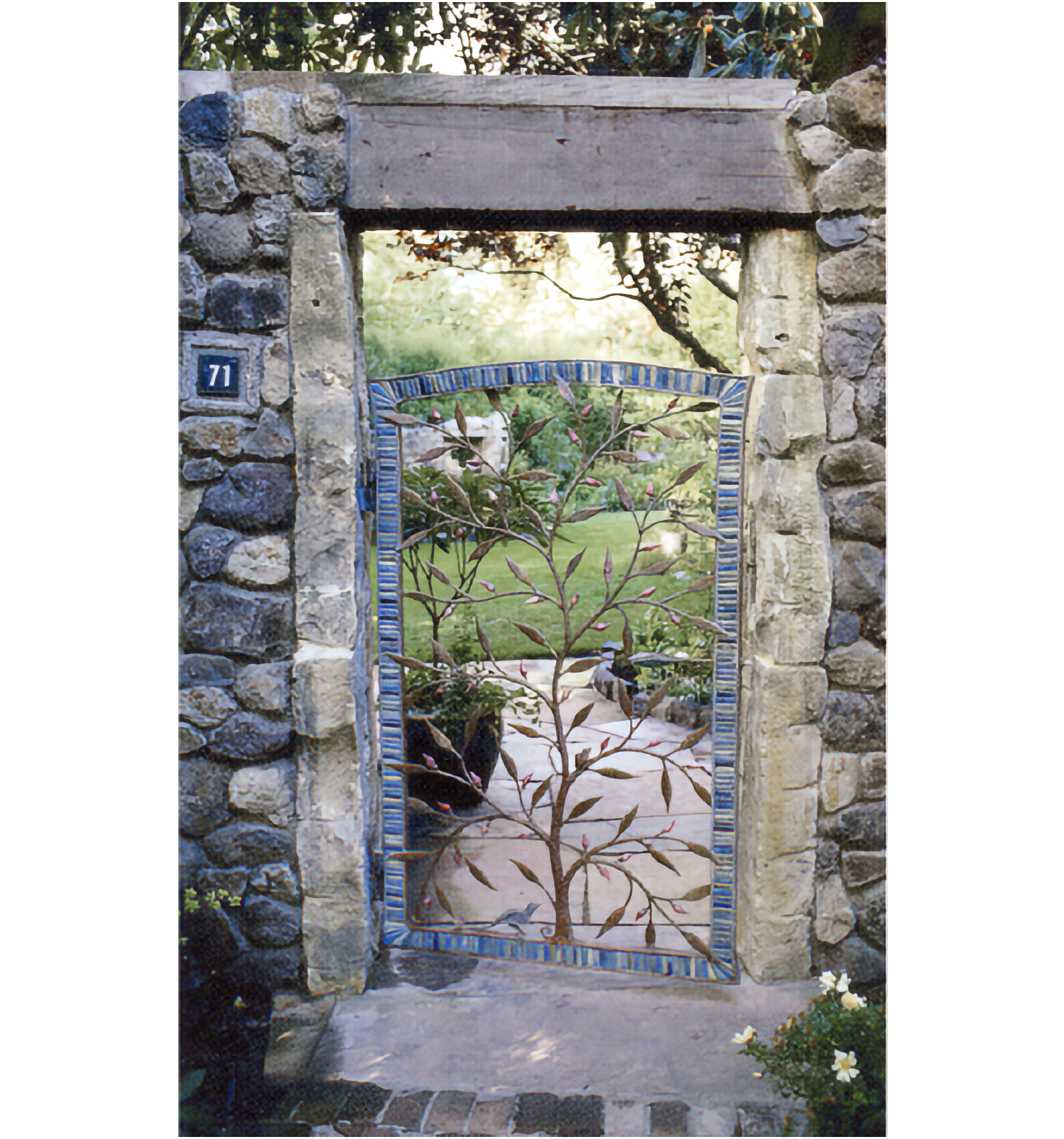 Photo of stone-sided garden entrance with wooden lintel, with a metal sculpture of a tree of life in a blue-tiled-bordered gate 