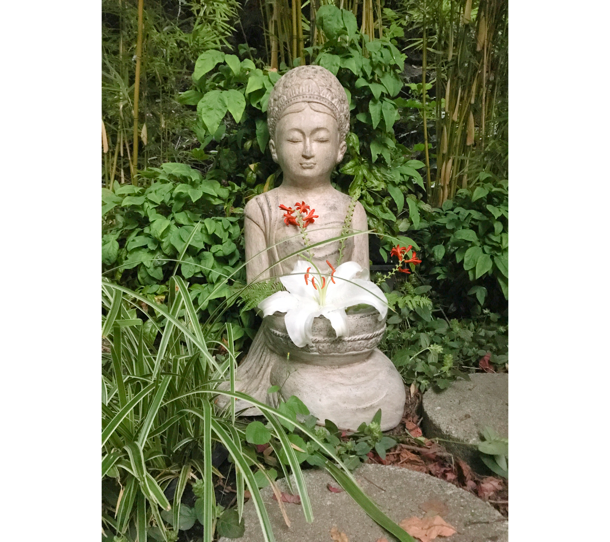 Small light grey cast of Kwan Yin, holding a live white stargazer lily blossom, surrounded by small green plants