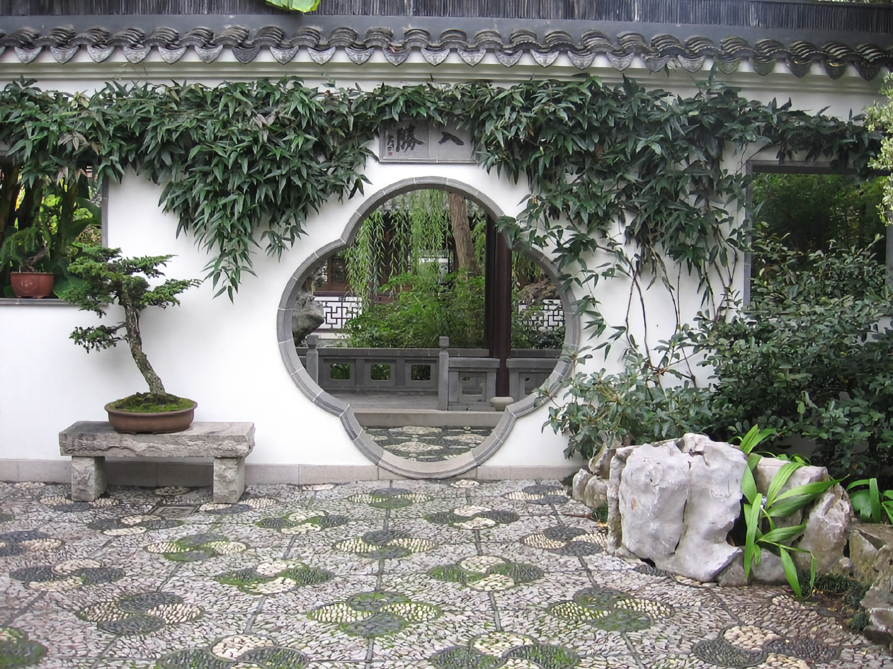 Photo of large curved space in white wall leading to a garden, with stone and grass mosaic patterns on the ground