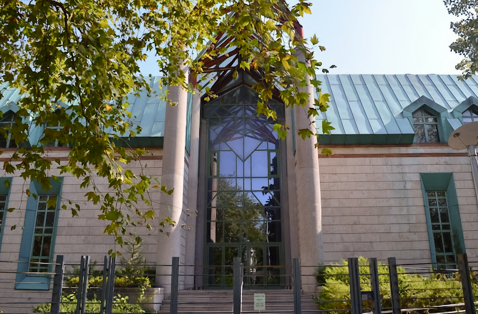 Photo  of front entrance of brown block building and blue roof with high vertical atrium topped by red pointed arches