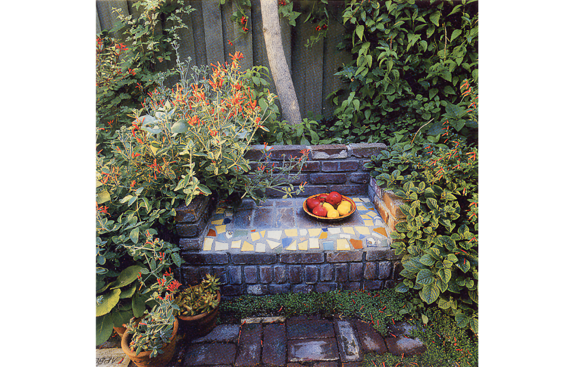 THere is a bowl of red and yellow fruit on the seat, and green plantings with small red flowers on either side, with a thin tree trunk and a fence in the back