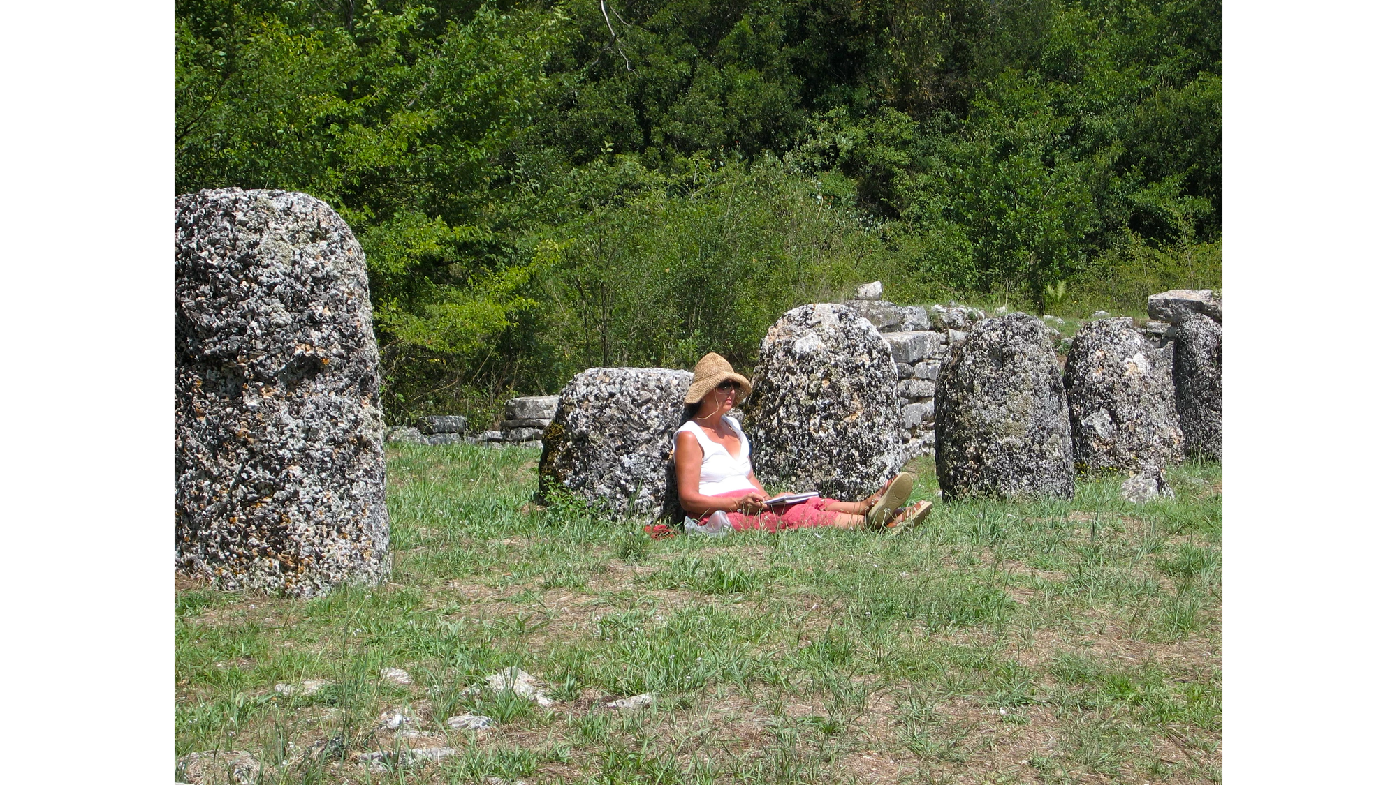 Photo os Sandra Dean sitting on ground leaning against ancient stone, sketching