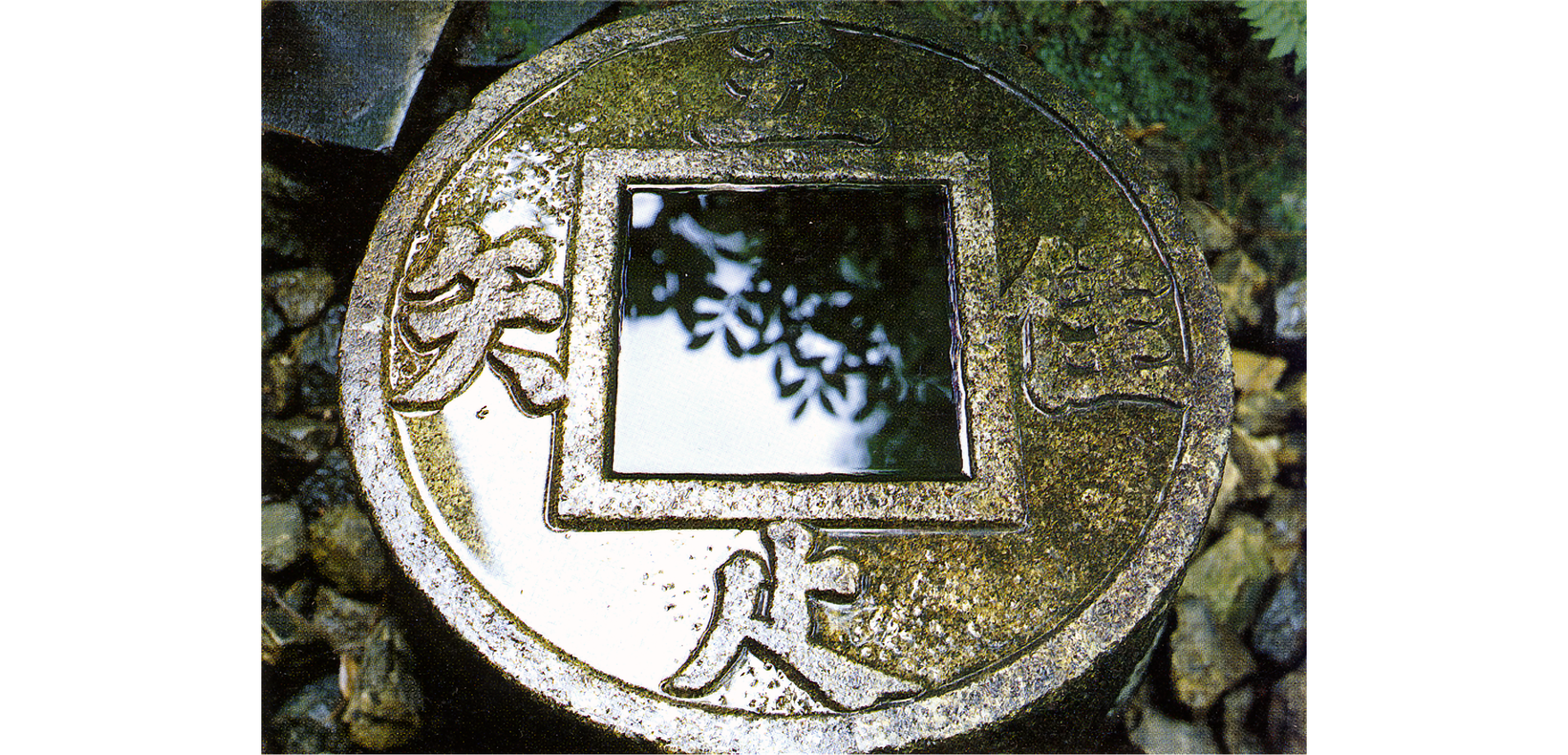 Round stone with Chinese characters, with square inset containing water and reflecting tree branches.