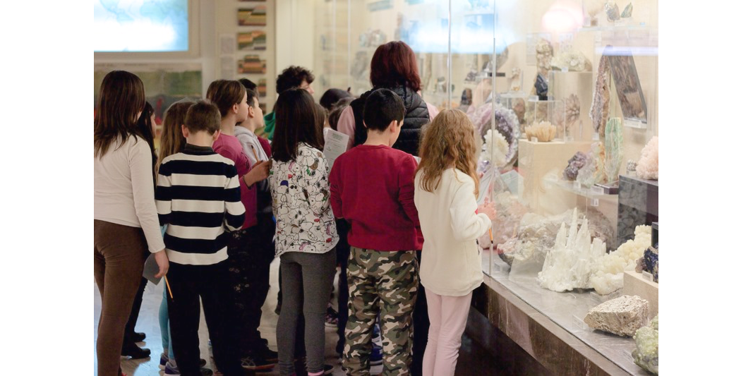 Photo of pre-teens and teacher in front of class case filled with shells