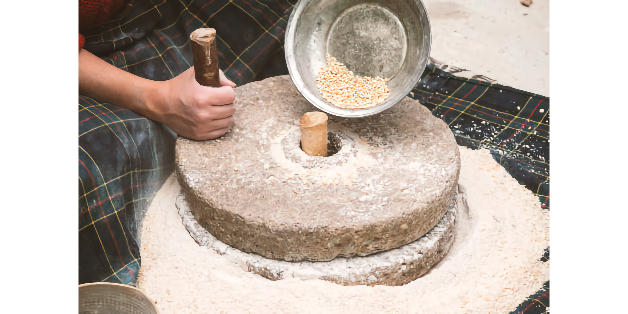 Photo of hand turning top of two stones to grind wheat into flour