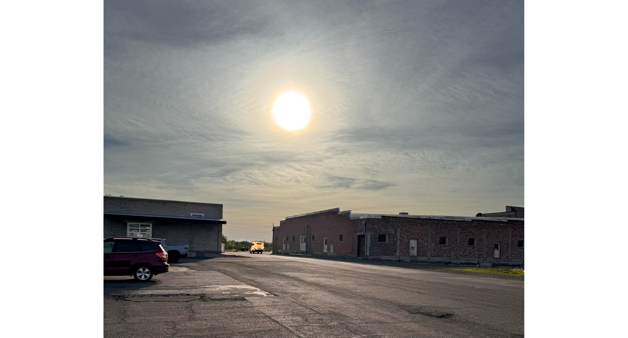 Photo of small yellow truck at end of road, in between two buildings, with sun above