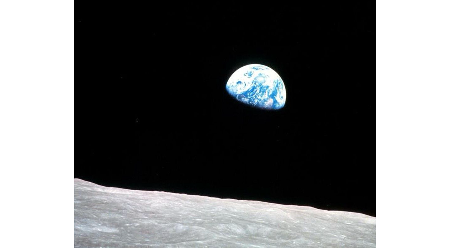 Photo from space of half blue earth rising above barren moon's surface.