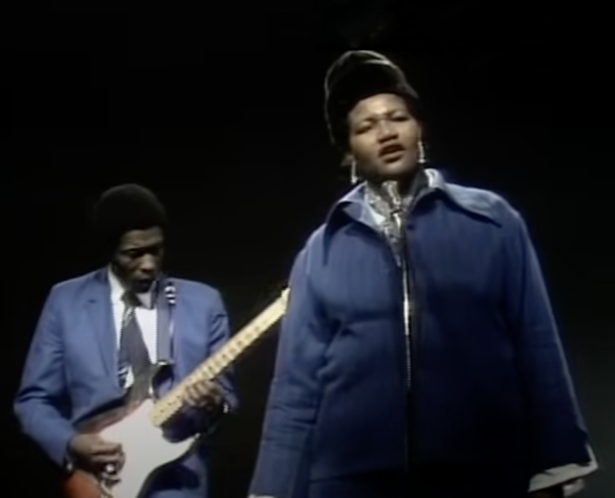 Video image of Big Mama Thornton singing with coat and hat on, with guitar player Buddy Guy behind her