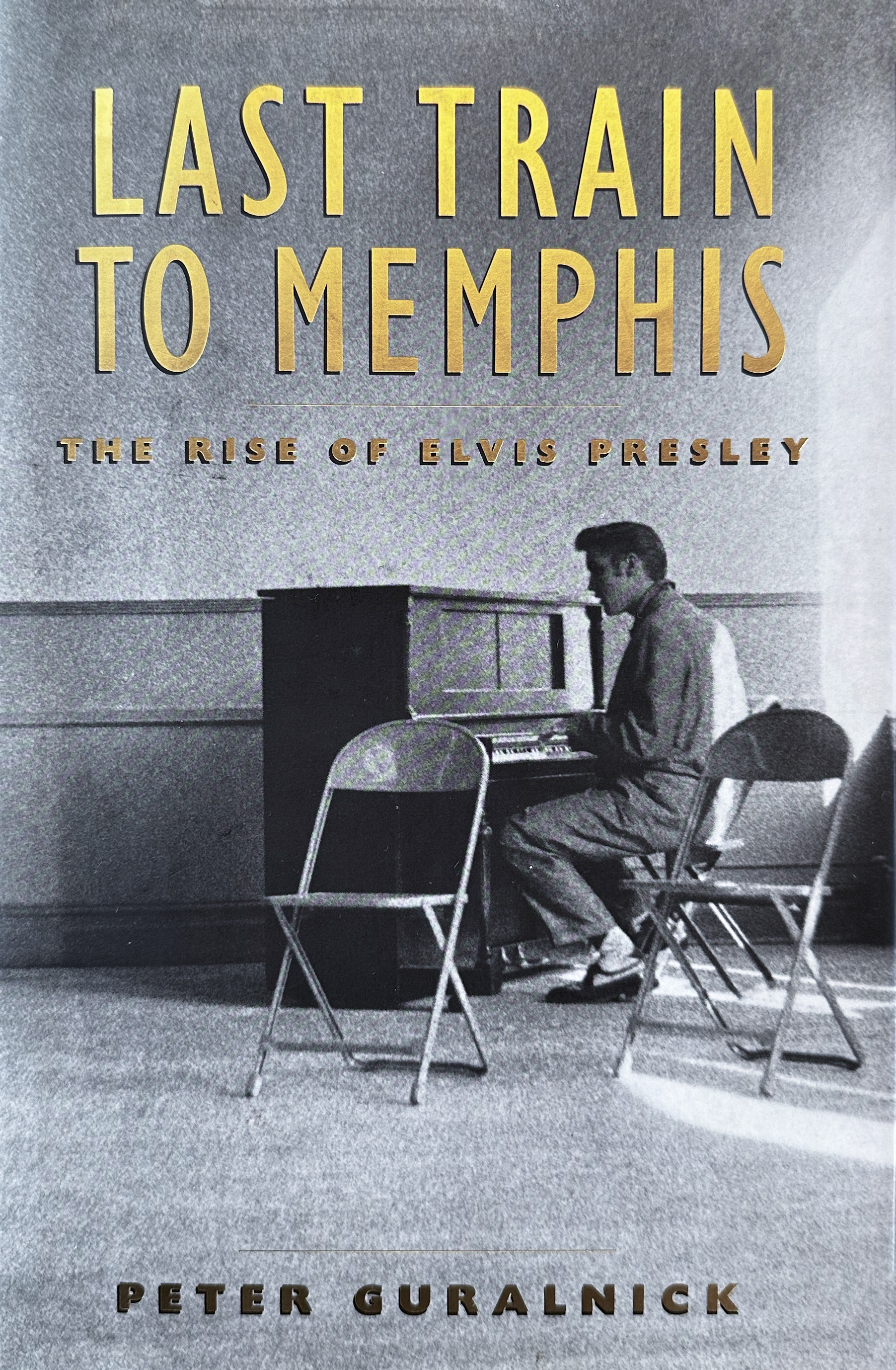 Image of cover of book, with Elvis alone in a room, playing an upright piano, and two empty chairs behind him.