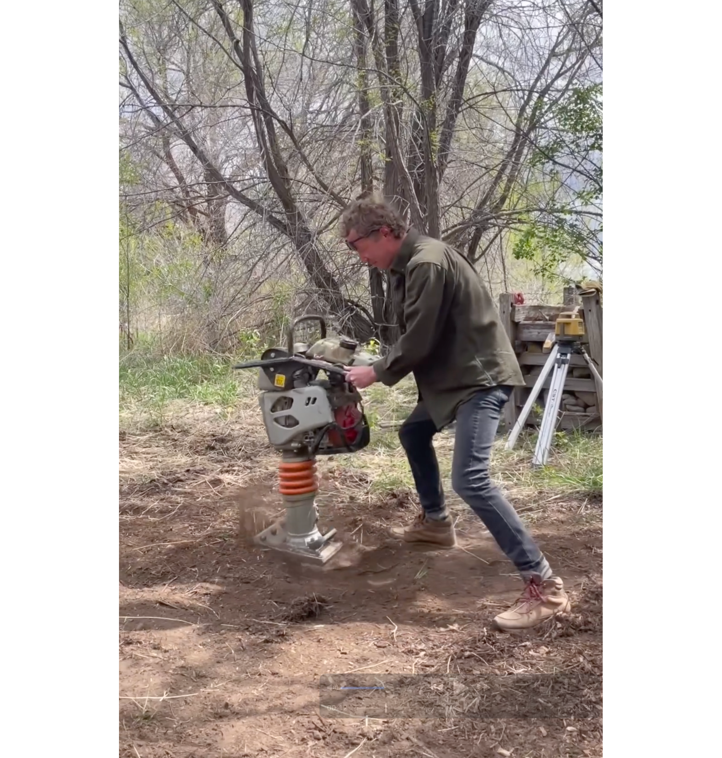 Photo of Nick operating a ground pound on bare soil, with a tree in the background.