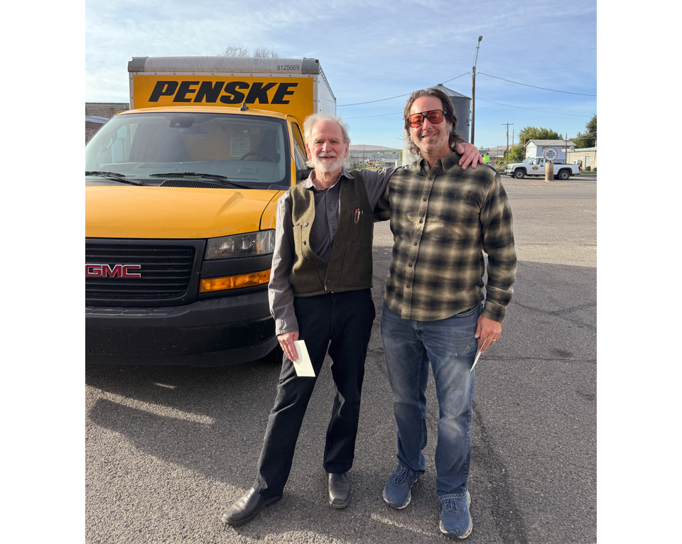 Photo of Trimpin and Troy Rogers arms on shoulders in front of yellow Penske truck